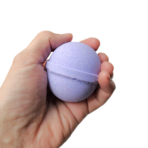 purple bath bomb with saturn ring held in palm of hand