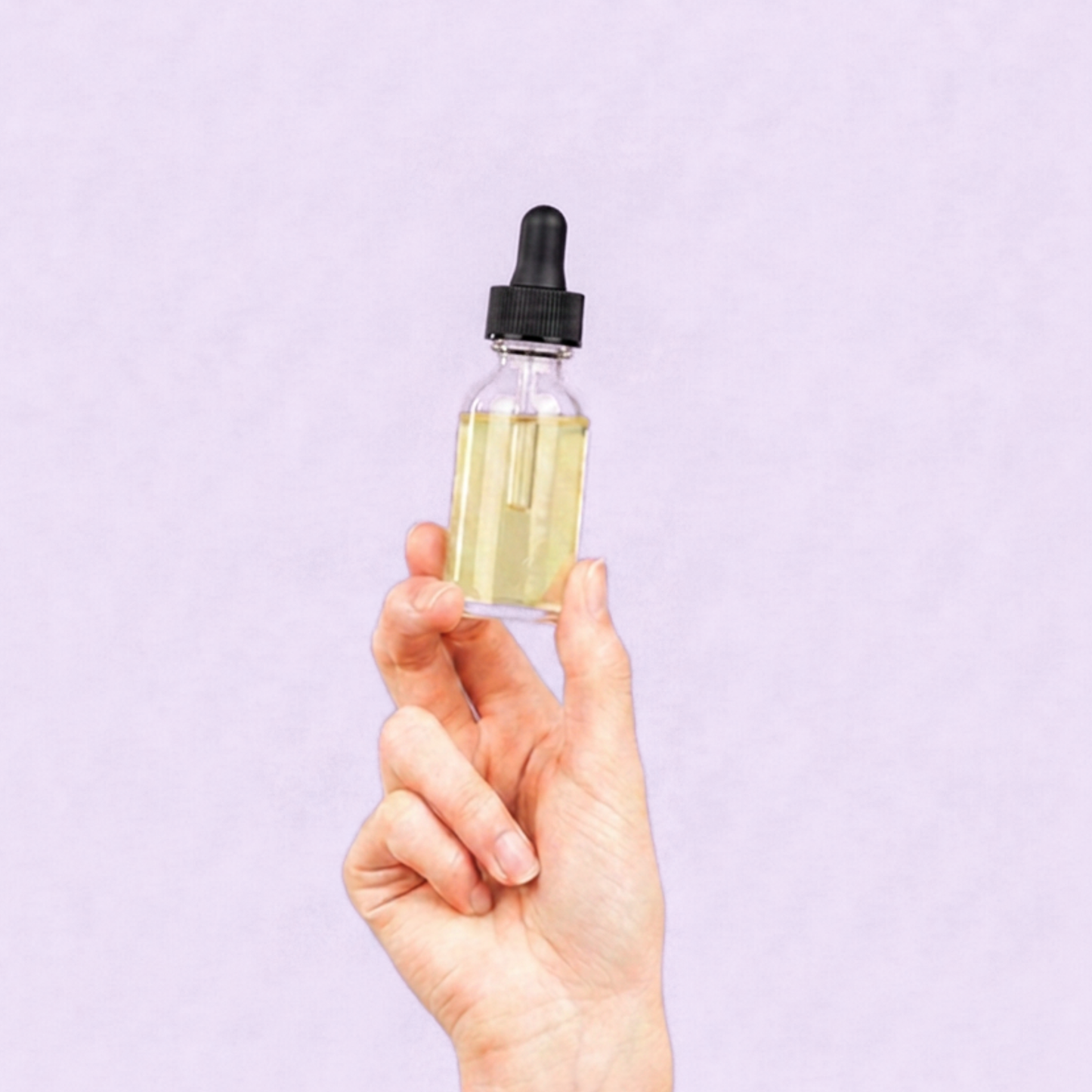 Hand holding a glass dropper bottle with a clear liquid against a light purple background