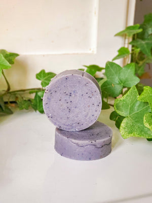 Two round purple palm free and vegan soaps with poppy seed additives stacked on top of each other.