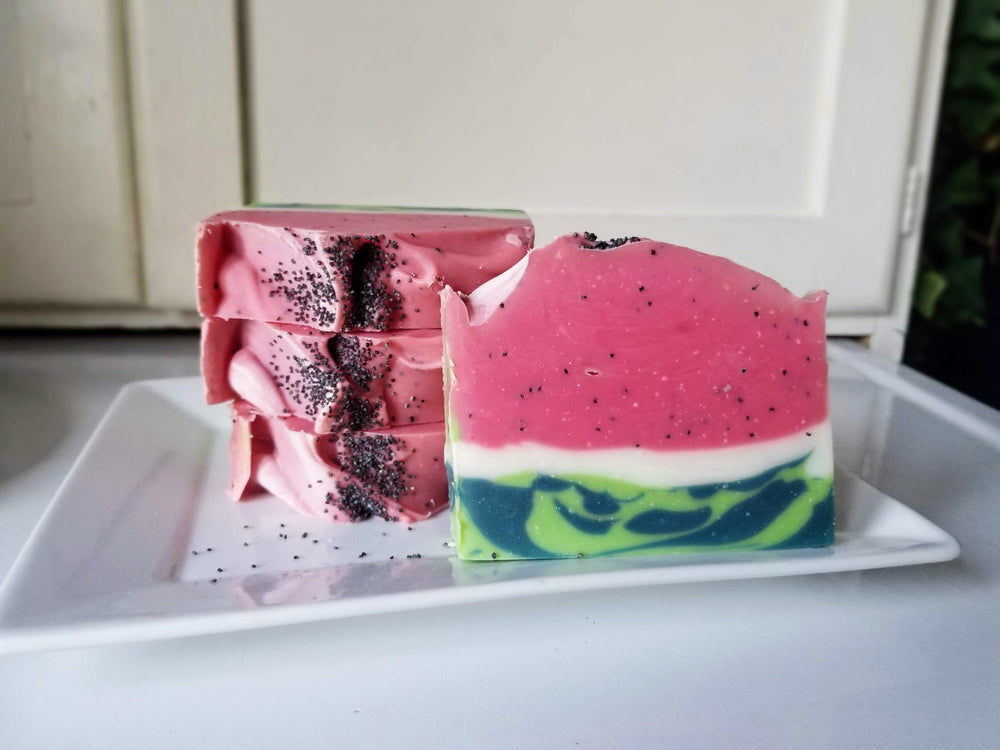 Bright pink watermelon bar soaps with poppyseeds stacked on a plate