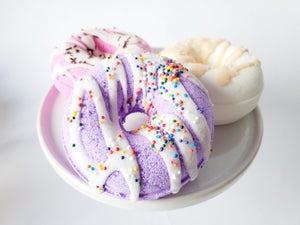 Purple vegan donut bath bomb with rainbow sprinkles on dessert tray